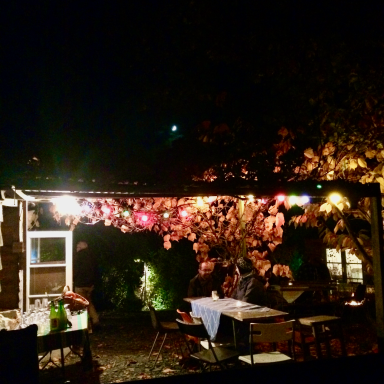 Gezellig restaurantterras met sfeervolle verlichting en bloemen bij nacht.